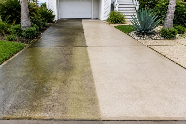 A driveway half cleaned, showing dark grime on one side and bright clean concrete on the other